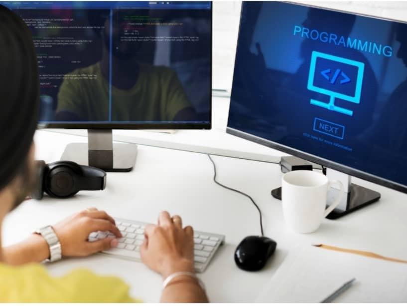 An photo shows a professional using two desktops and keyboard for programming in Python utilizing method overriding.